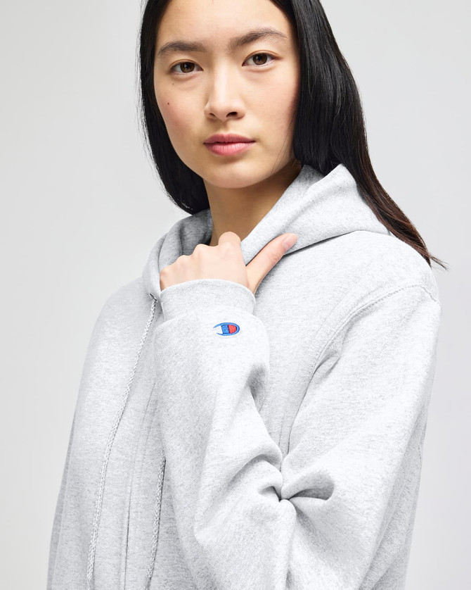 A grey full-zip hooded sweatshirt with a logo on the sleeve, featuring a model wearing it.