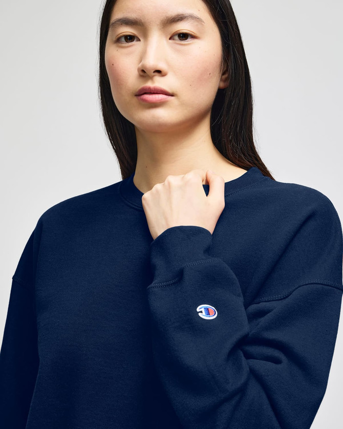 A navy blue women's crewneck sweatshirt with a logo on the sleeve, featuring a relaxed fit.