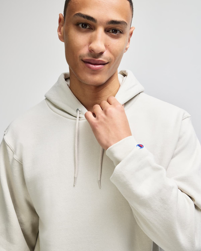 A light grey pullover hooded sweatshirt featuring a logo on the sleeve. Model wears it with a confident expression.