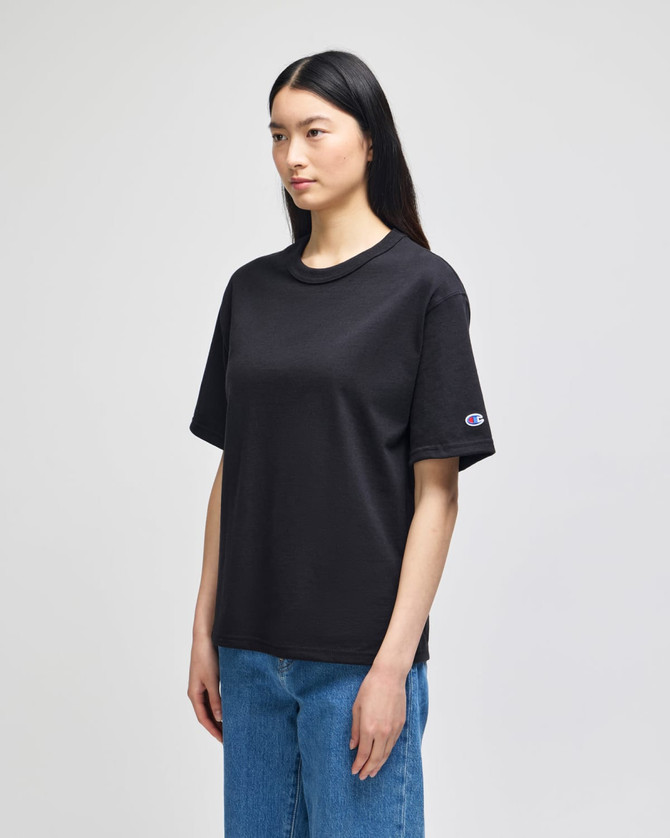 A black Champion Adult Heritage Jersey T-Shirt displayed on a model, featuring a logo on the sleeve.