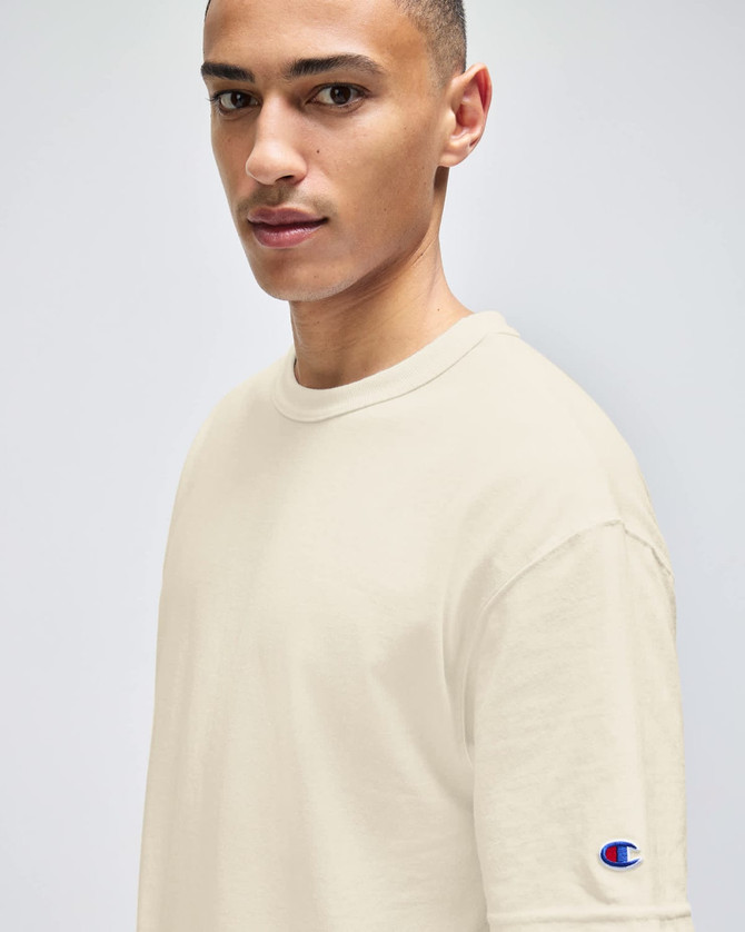A light beige t-shirt on a model, featuring a small logo on the sleeve.