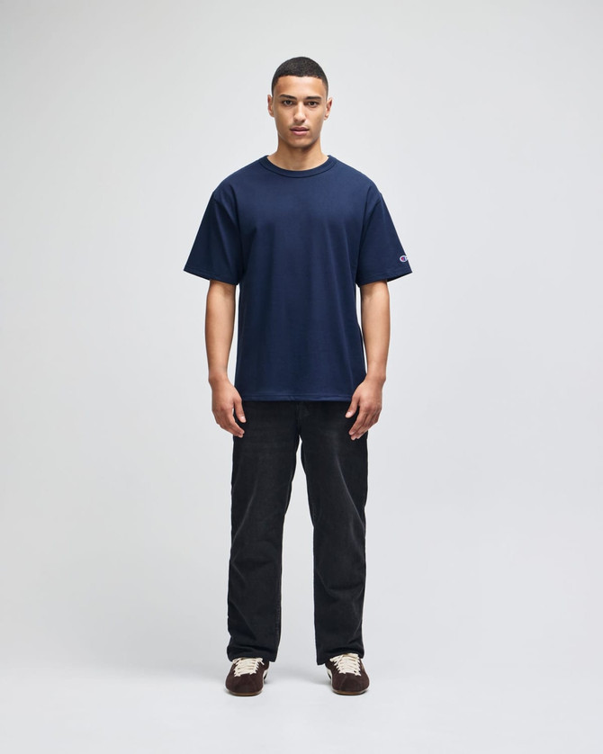 A navy t-shirt with short sleeves on a male model, paired with black pants. The shirt features a logo.