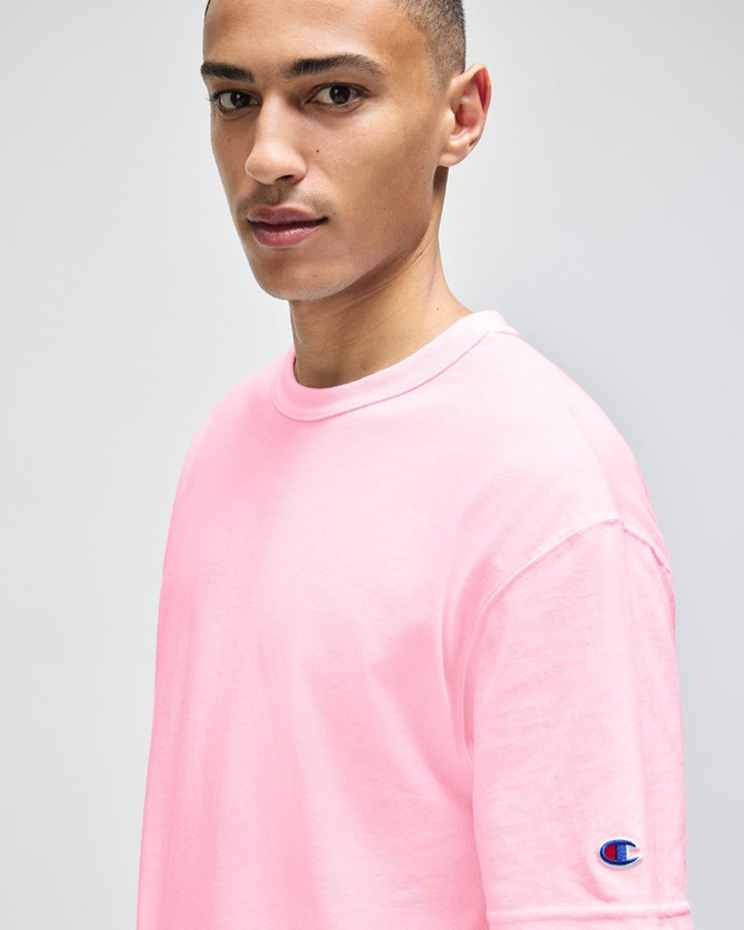 A pink Champion Adult Heritage Jersey T-Shirt displayed on a model, featuring a logo on the sleeve.