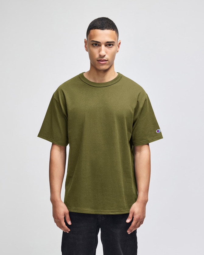 An olive green Champion Adult Heritage Jersey T-Shirt displayed on a model, featuring a logo on the sleeve.