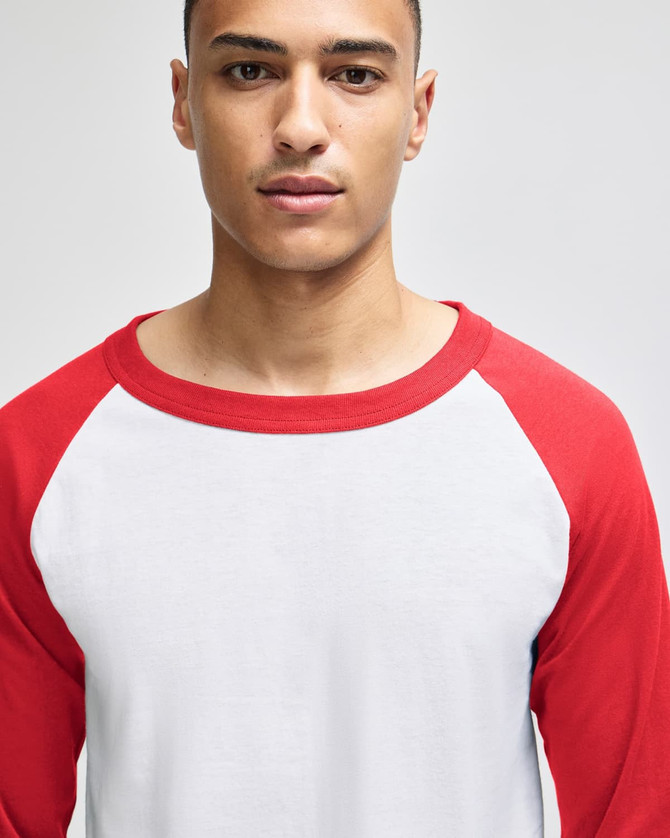 A model wearing a white and red raglan baseball T-shirt with three-quarter sleeves, paired with dark pants.