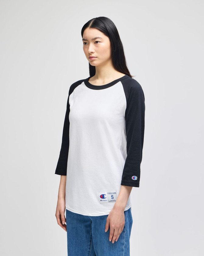 A black and white Champion Adult Raglan Baseball T-Shirt with long sleeves, featuring a logo on the hem.
