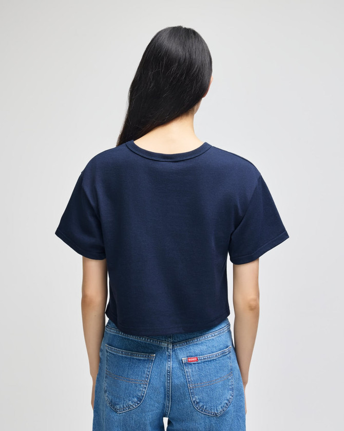 A navy cropped short sleeve t-shirt with a simple design and a logo on the back, worn with blue jeans.