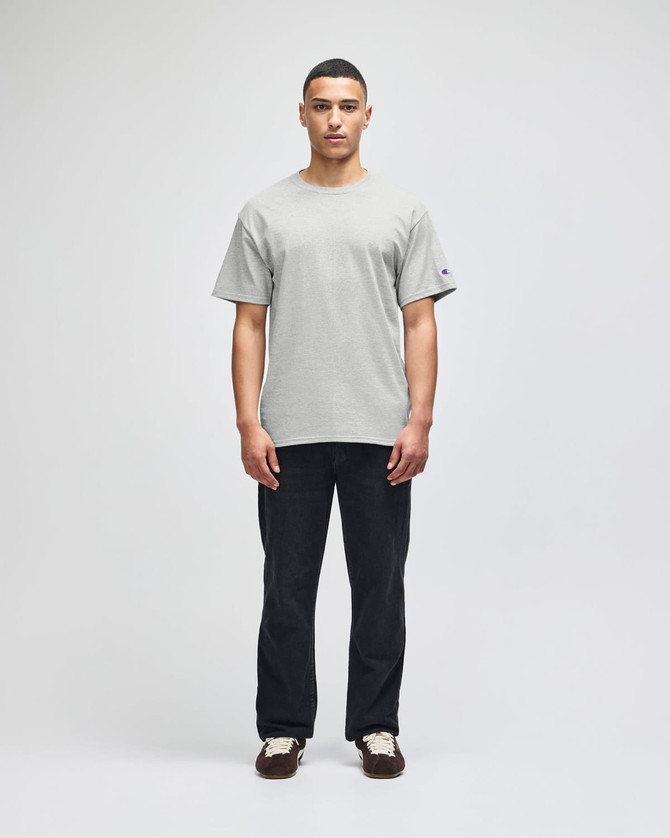 A short-sleeve t-shirt in grey with a logo, modelled by a man, paired with black trousers.