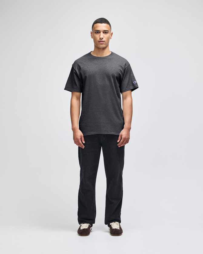 A model wearing a grey Champion adult short-sleeve T-shirt paired with black pants. The shirt features a logo.