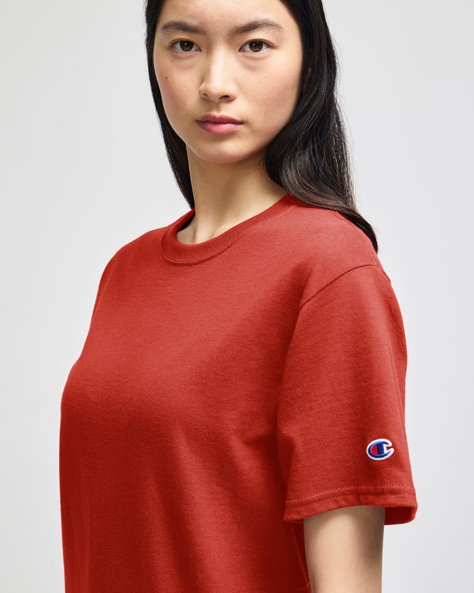 A red Champion adult short-sleeve T-shirt with a logo on the sleeve, displayed on a model.