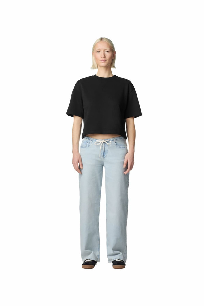 A black mid-length boxy top paired with light blue trousers, worn by a model standing upright. The outfit features a casual style.
