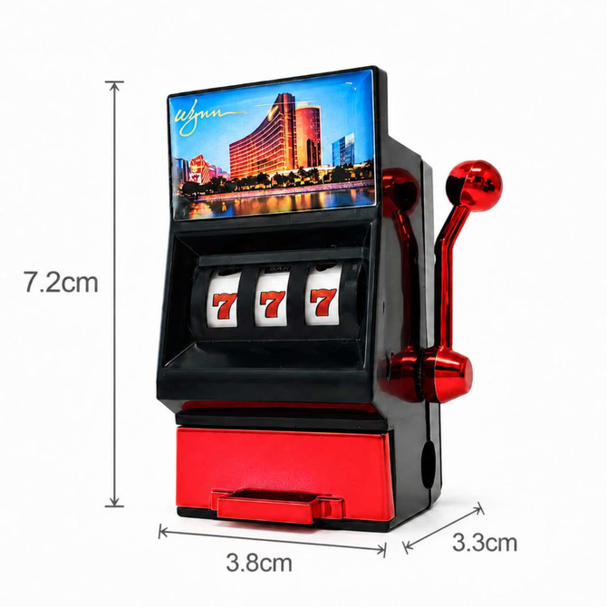 A red and black fridge magnet resembles a slot machine, featuring three spinning reels with sevens and a decorative building image.