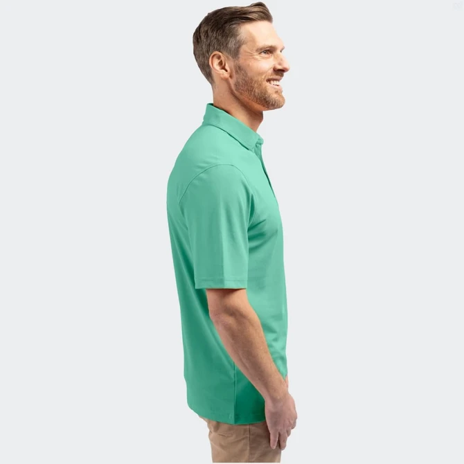 A man in a green polo shirt stands smiling, with a logo on the shirt's chest.