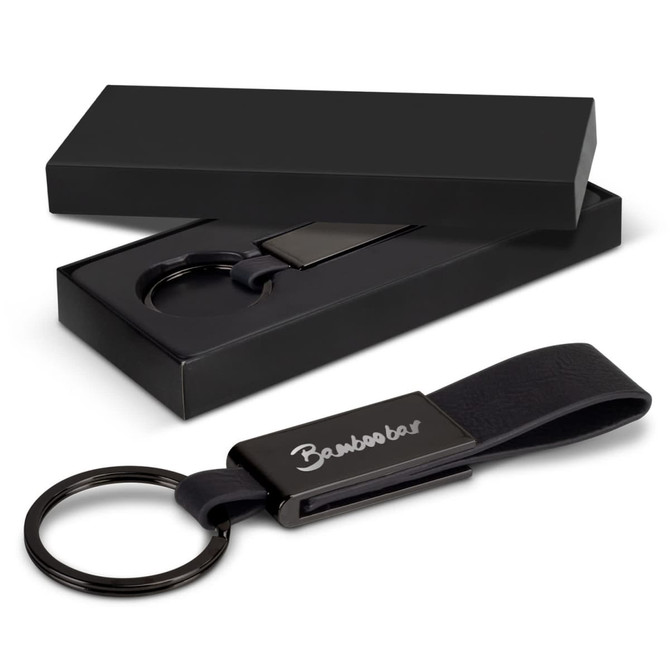 A black key ring with a leather strap and metal clip, displayed in a sleek black box.