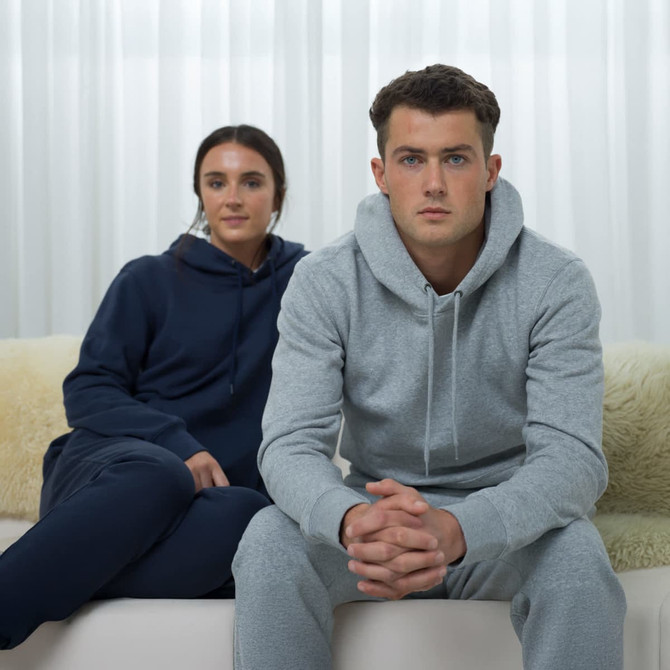 A pair of unisex sweatpants in navy and grey, styled with matching hoodies, on individuals seated indoors.