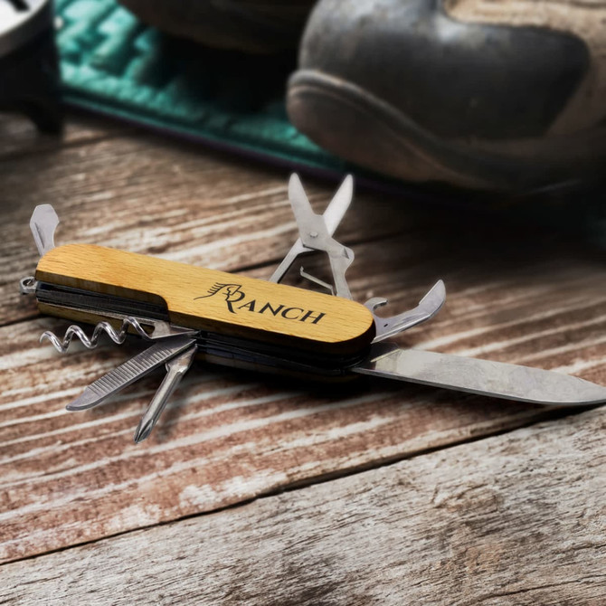 A wooden pocket knife with multiple tools, featuring a corkscrew and blade, set on a wooden surface.