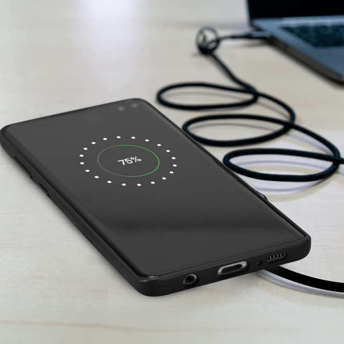 A black smartphone on a desk, charging wirelessly with a visible battery percentage. A charging cable is nearby.