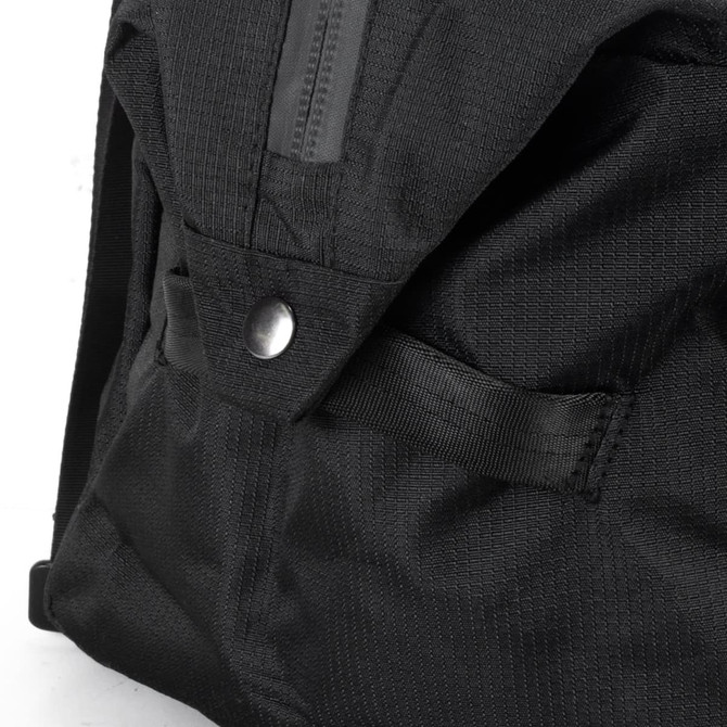 A close-up of a black duffle bag featuring fabric texture and a snap button closure. It has a logo on the side.