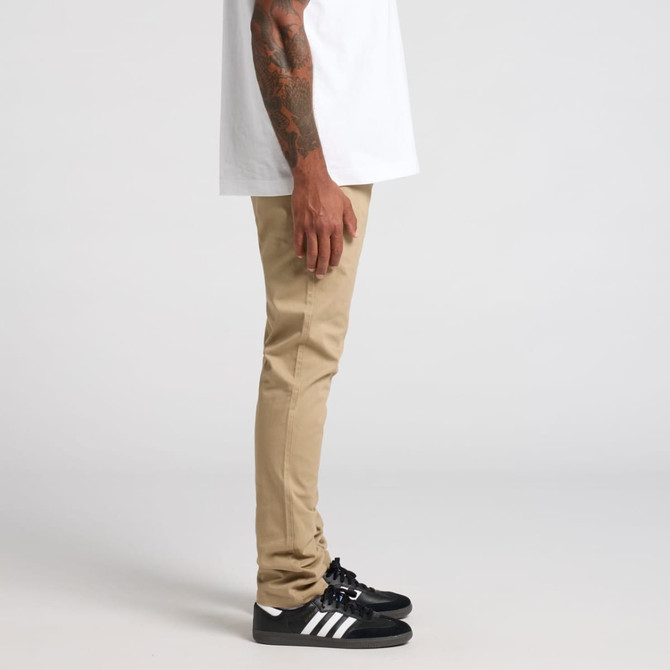 A pair of khaki standard pants displayed on a model, paired with black shoes and a white shirt.