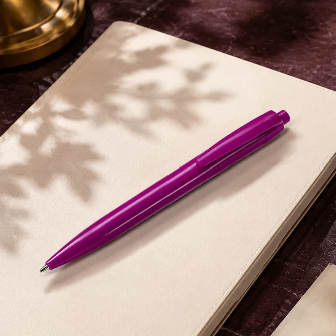 A purple plastic pen resting on an open notebook, with soft shadows in the background.