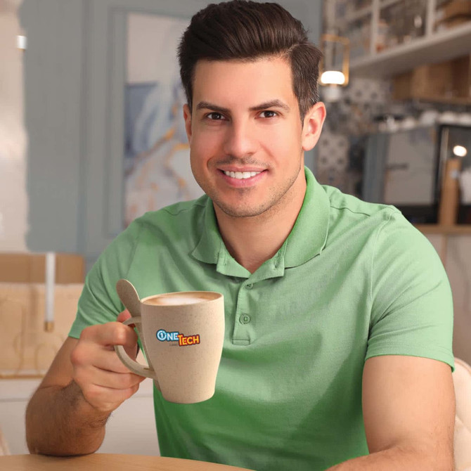 A wheat fibre cup in a light color with a matching spoon, held by a smiling man in a green polo shirt.