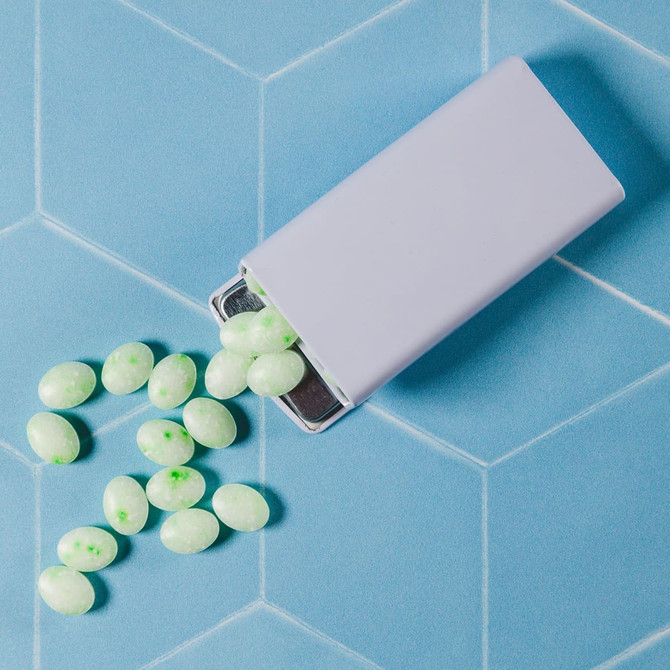 A flip top tin containing spearmint mints, featuring light green and white confections scattered on a blue background.