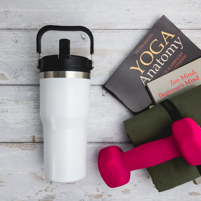 A drink bottle in white with a black lid and handle, beside a yoga book, mat, and pink dumbbells.