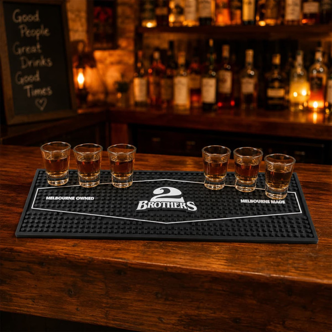 A black moulded PVC bar runner with five shot glasses arranged on it, set against a wooden bar backdrop.