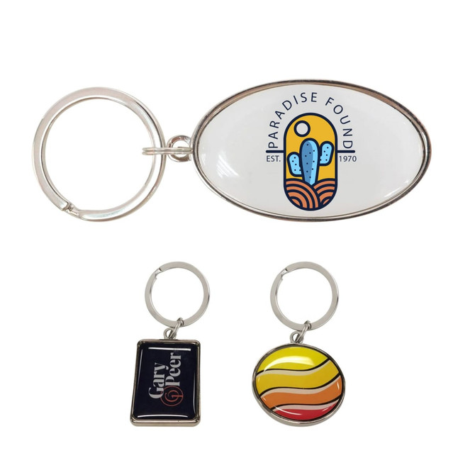 A custom-shaped metal keyring in silver, featuring an oval design with a colourful logo, alongside two smaller keyrings.