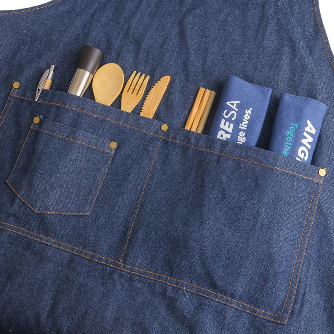 A denim blue bib apron featuring multiple pockets with wooden utensils and cloth napkins neatly arranged.