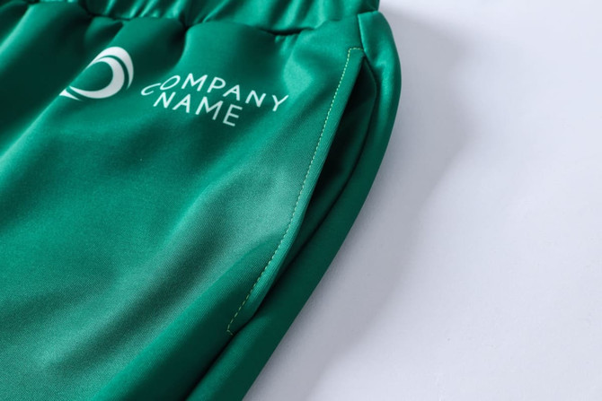 Green unisex adult sports shorts made from 100% polyester, featuring a side pocket and a logo.