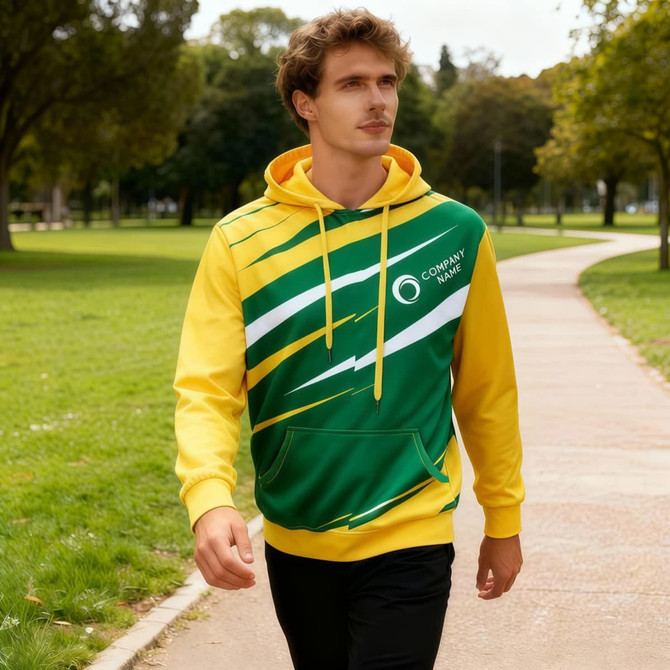 A unisex hoodie featuring green and yellow colours, with a logo, worn by a man walking in a park.