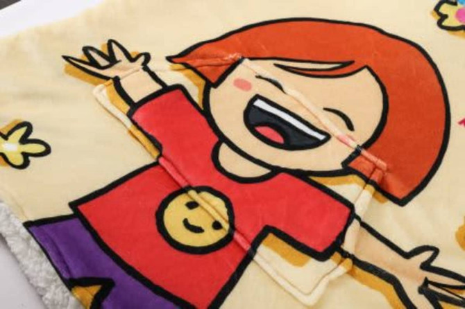 A wearable blanket featuring a cheerful cartoon character with a red shirt, yellow smiley face, and vibrant designs.