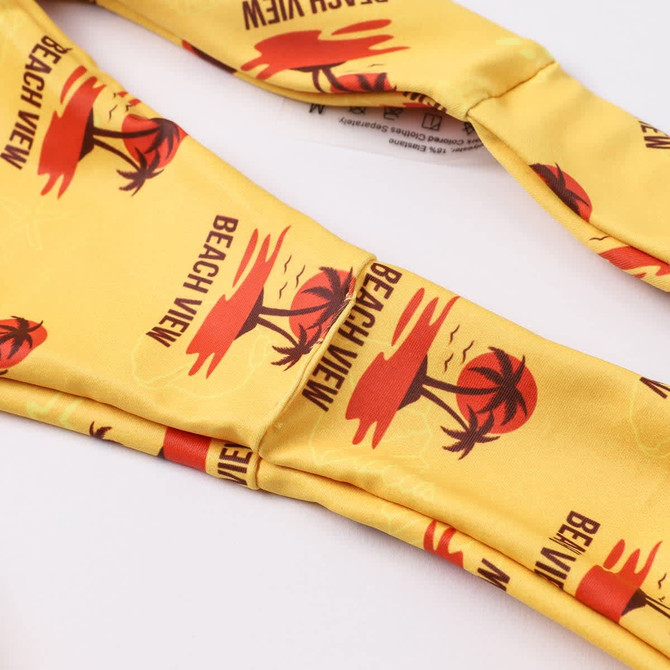 A yellow bikini bottom featuring a palm tree print, with red accents and a logo.
