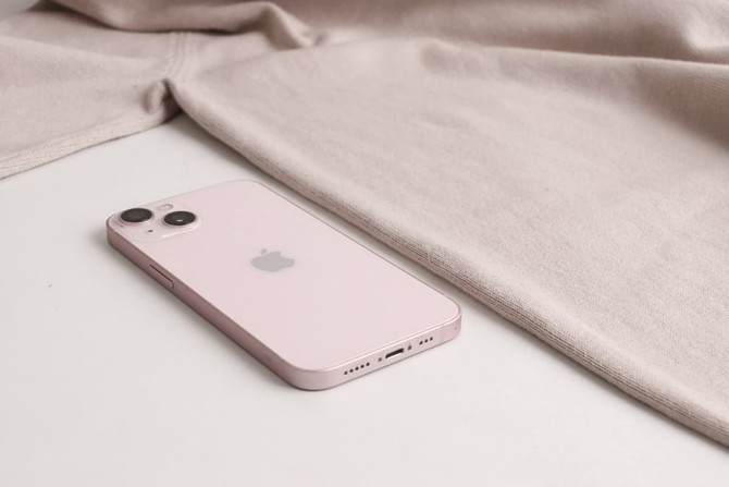 A light beige crew neck sweater next to a pink smartphone with an Apple logo.