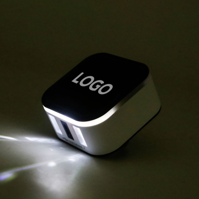 A travel adapter in black and white with USB ports and a logo on the top.