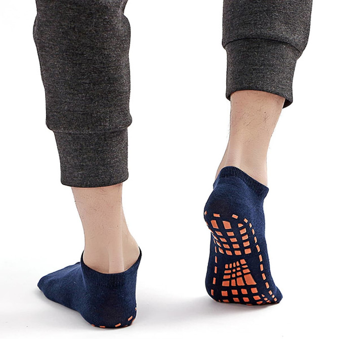 Low cut kids gripper socks in navy blue with orange grip dots on the sole, displayed from the back on a model's feet.
