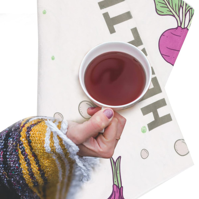 A tea towel featuring a vibrantly patterned design in shades of cream, with a hand holding a cup of tea.