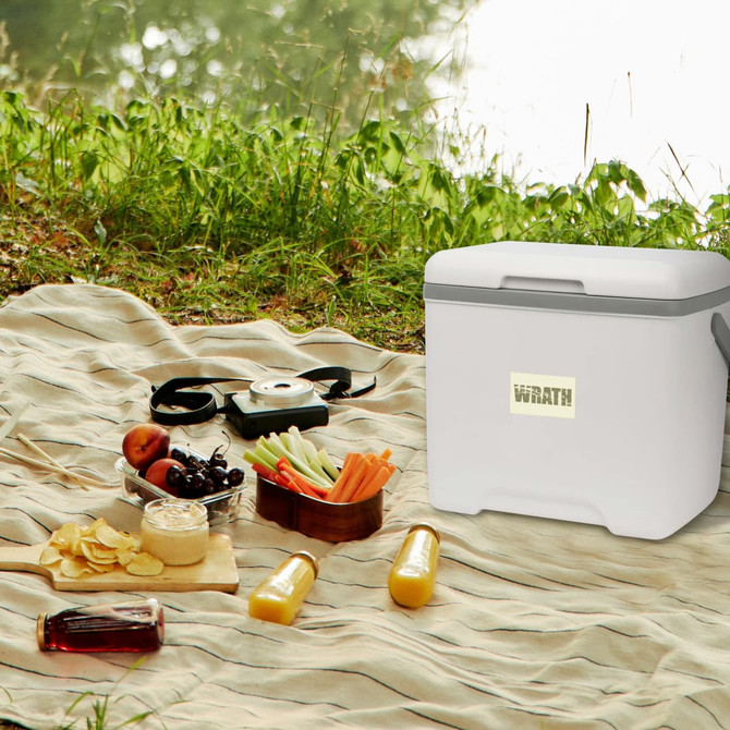 A white cooler box with a grey handle sits on a picnic blanket, surrounded by food and drinks. There is a logo on the box.
