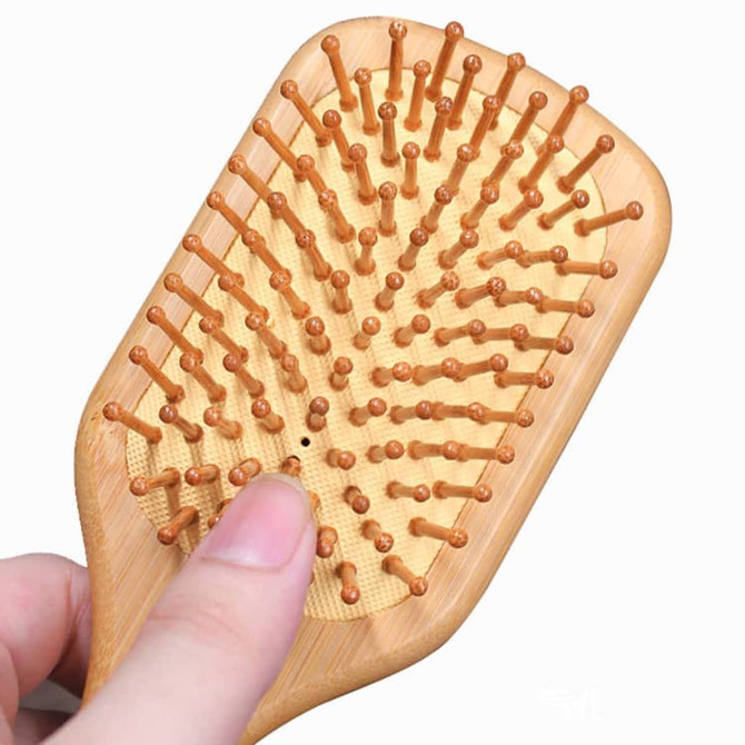 A bamboo hair brush featuring wooden pins and a natural finish, held in a hand.