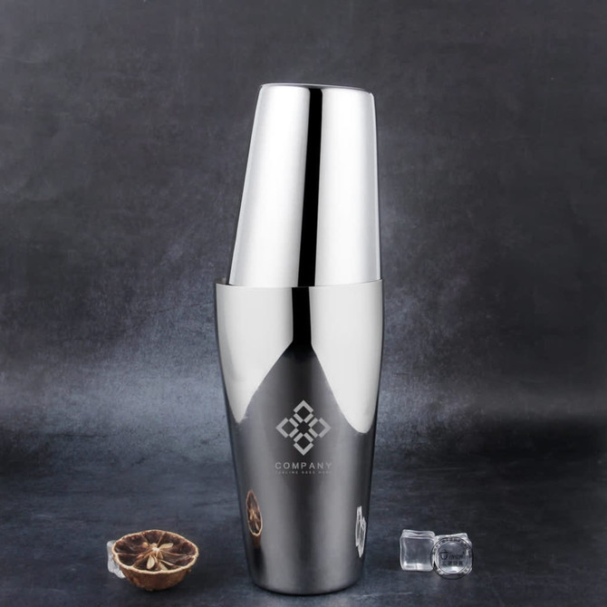 A stainless steel cocktail shaker in shiny silver, featuring two sizes, alongside ice cubes on a dark background.
