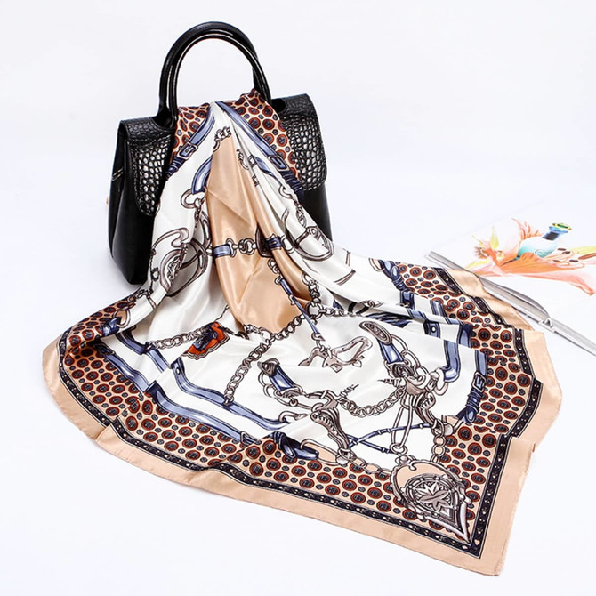 A silk satin scarf featuring a cream and beige pattern, displayed next to a black bag and a magazine.