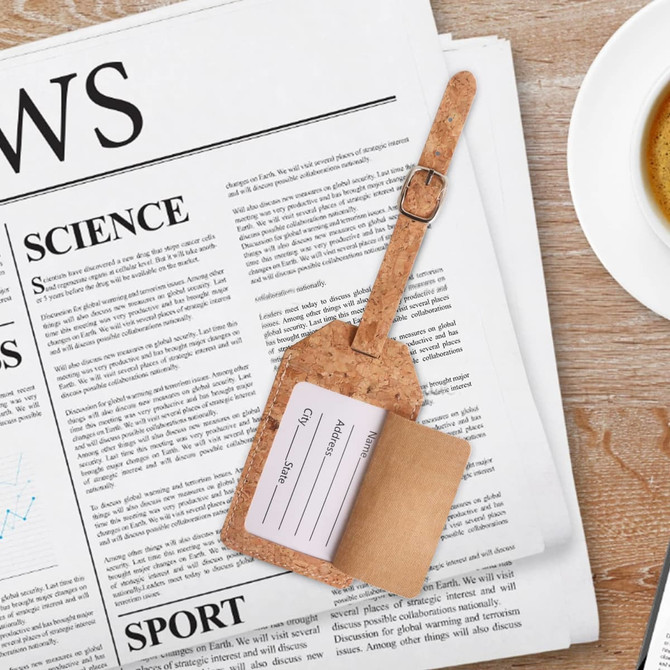 A cork luggage tag in natural tones, featuring a fold-out section for personal information, resting on a newspaper.