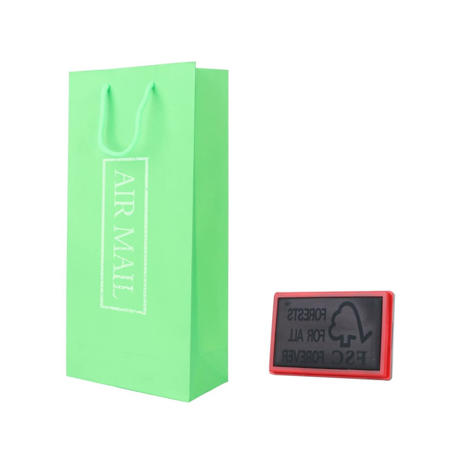 A green paper bag with handles alongside a red stamp, featuring a logo and text.