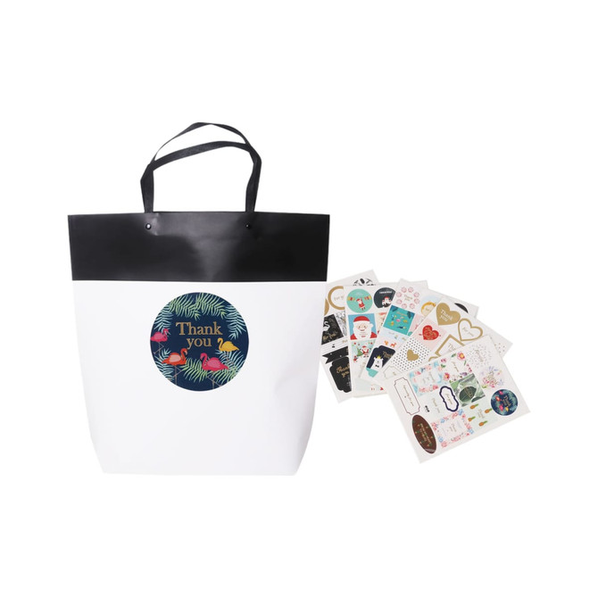 A large black and white boutique paper bag with a black handle, accompanied by assorted decorative stickers.