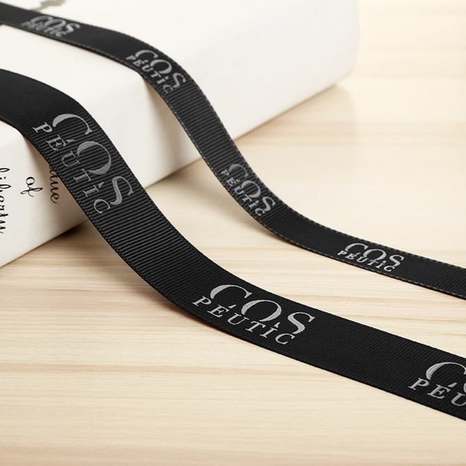 A black ribbed fabric ribbon with a logo, laid across a light surface next to a package.
