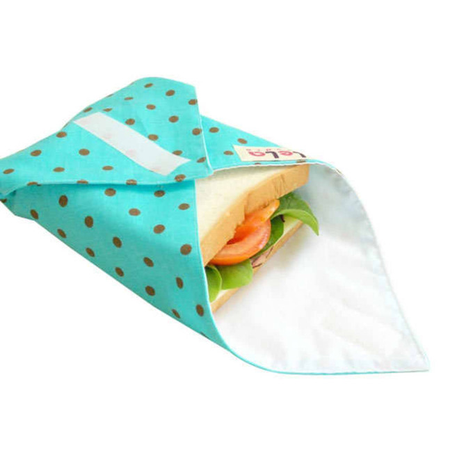 A reusable food wrap in aqua with white polka dots, partially covering a sandwich with lettuce and tomato.