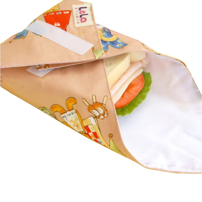A reusable food wrap featuring a colourful design with animals, holding a sandwich with lettuce and tomato.