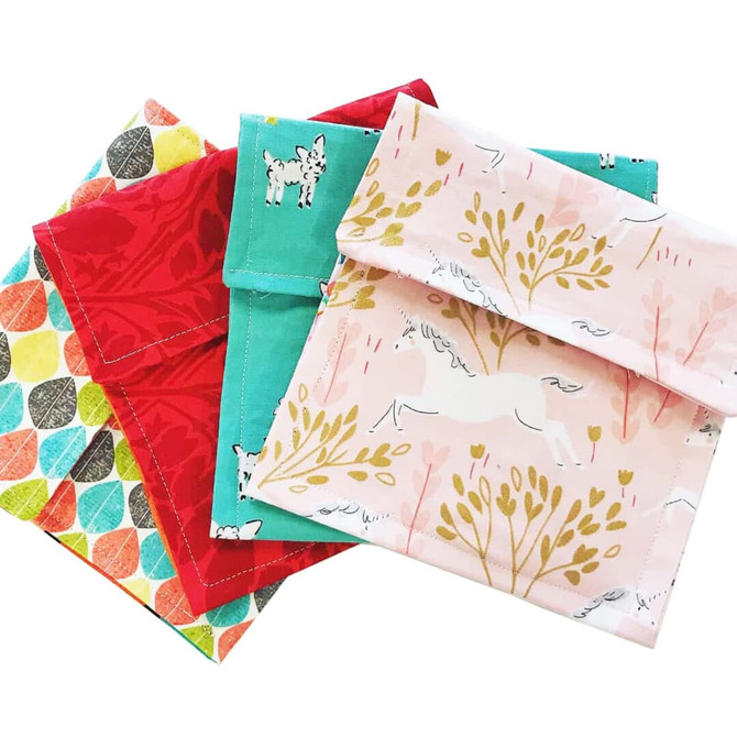 A set of four reusable food pouches in red, teal, pink, and patterned designs, featuring a Velcro closure and various prints.