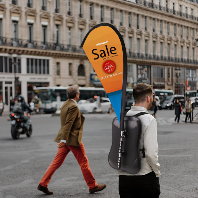 A black teardrop backpack with a flag attachment, displayed in an urban setting, featuring a logo.